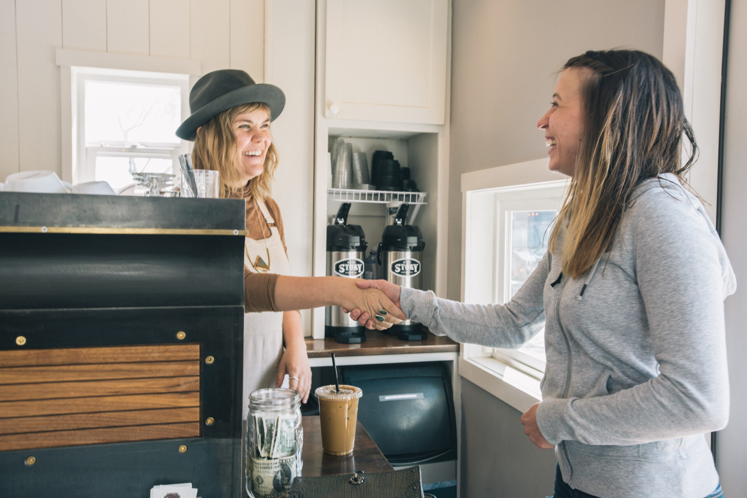 Two women shake hands at Story Coffee Co, one of the many women owned businesses in Colorado Springs