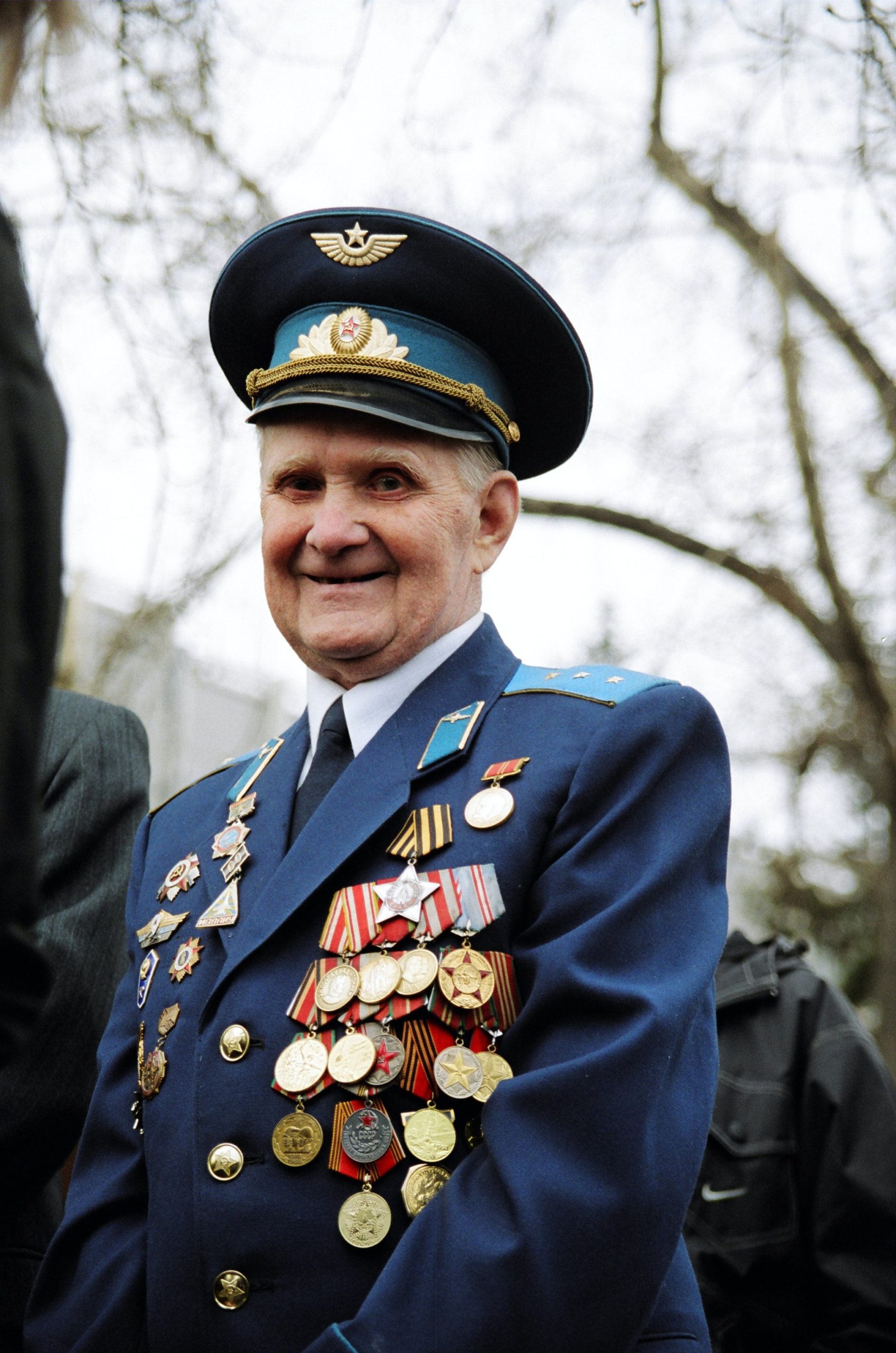 An older man in military uniform covered in medals smiles at the camera.