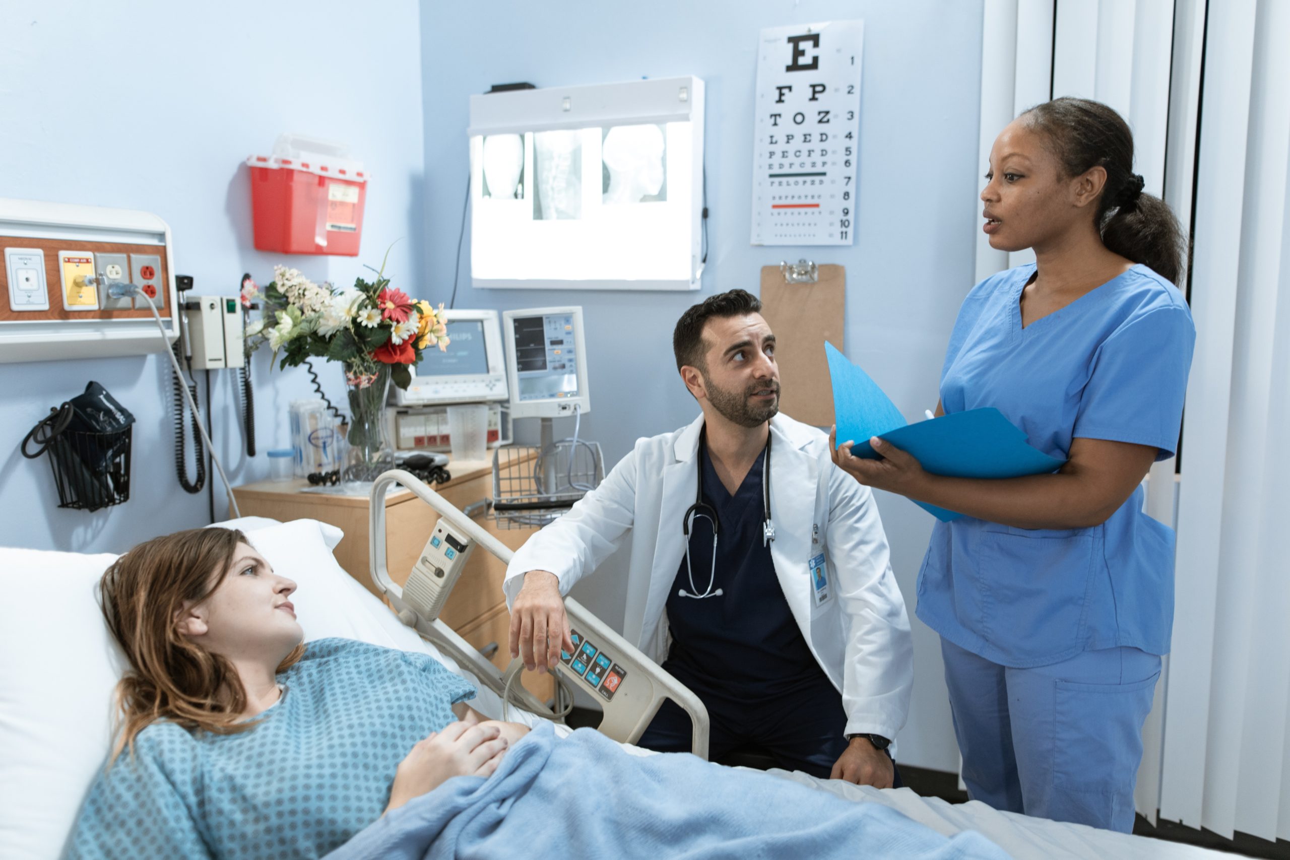 Two doctors talk to a patient in a hospital bed.