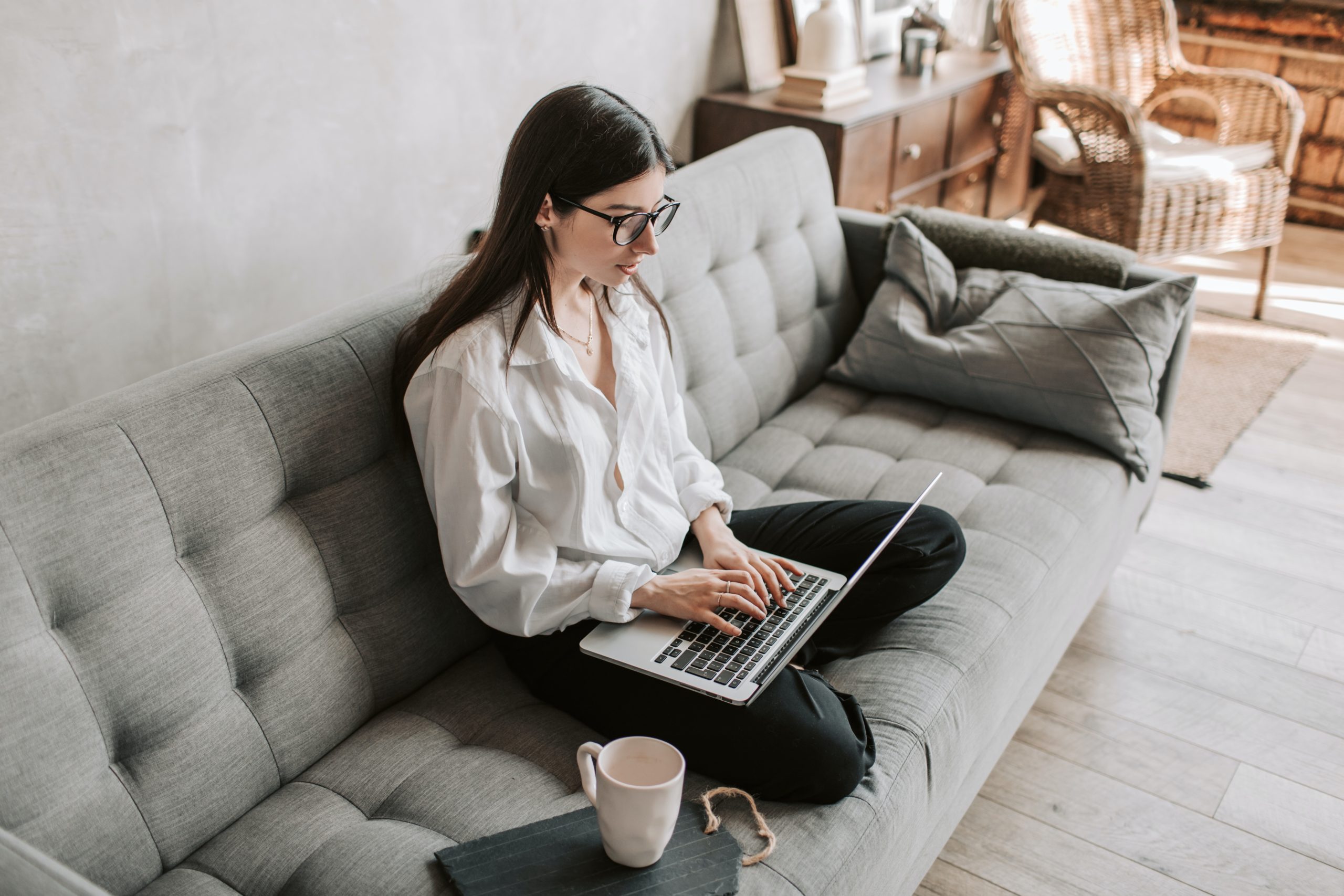 A woman sitting on a couch works on a laptop.