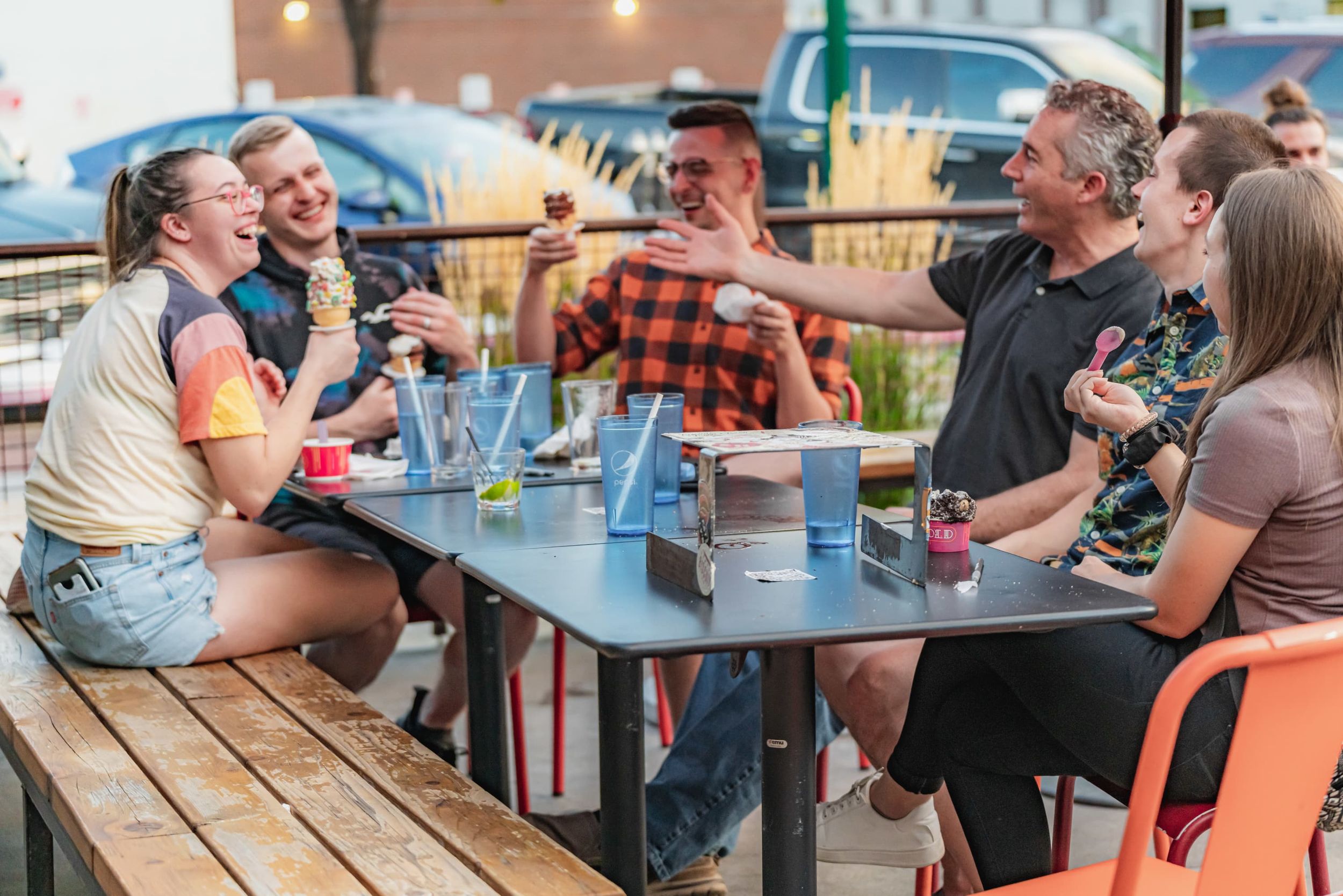 A group of people laugh while eating ice cream at an outdoor table.